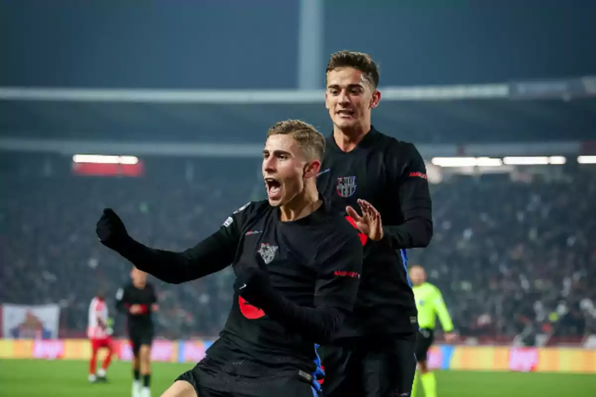 Dos jugadores de fútbol celebran un gol en un estadio lleno de espectadores.