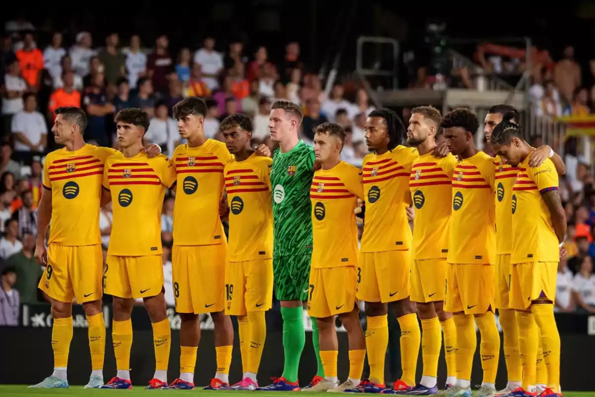 Jugadores de fútbol del FC Barcelona con uniforme amarillo y rojo, alineados y abrazados antes de un partido.