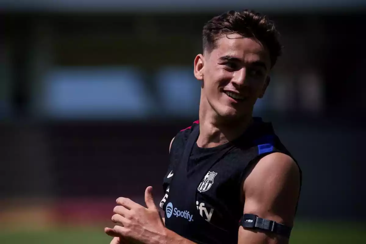 A soccer player smiles during training, wearing a sleeveless FC Barcelona shirt with the Spotify logo. A soccer player smiles during training, wearing a sleeveless FC Barcelona shirt with the Spotify logo.