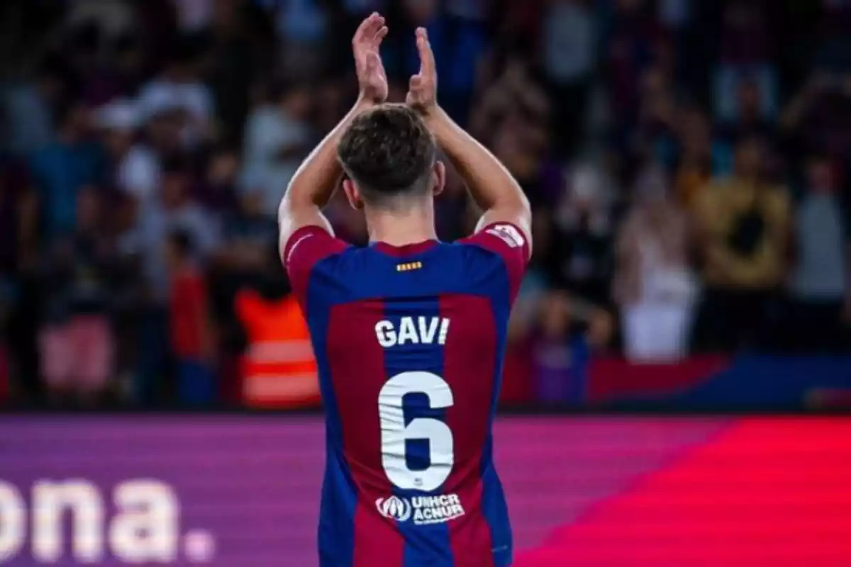 Se puede ver a Gavi, de espaldas, con la primera camiseta del Barcelona. Tiene los brazos en alto, con las manos en posición de aplaudir.