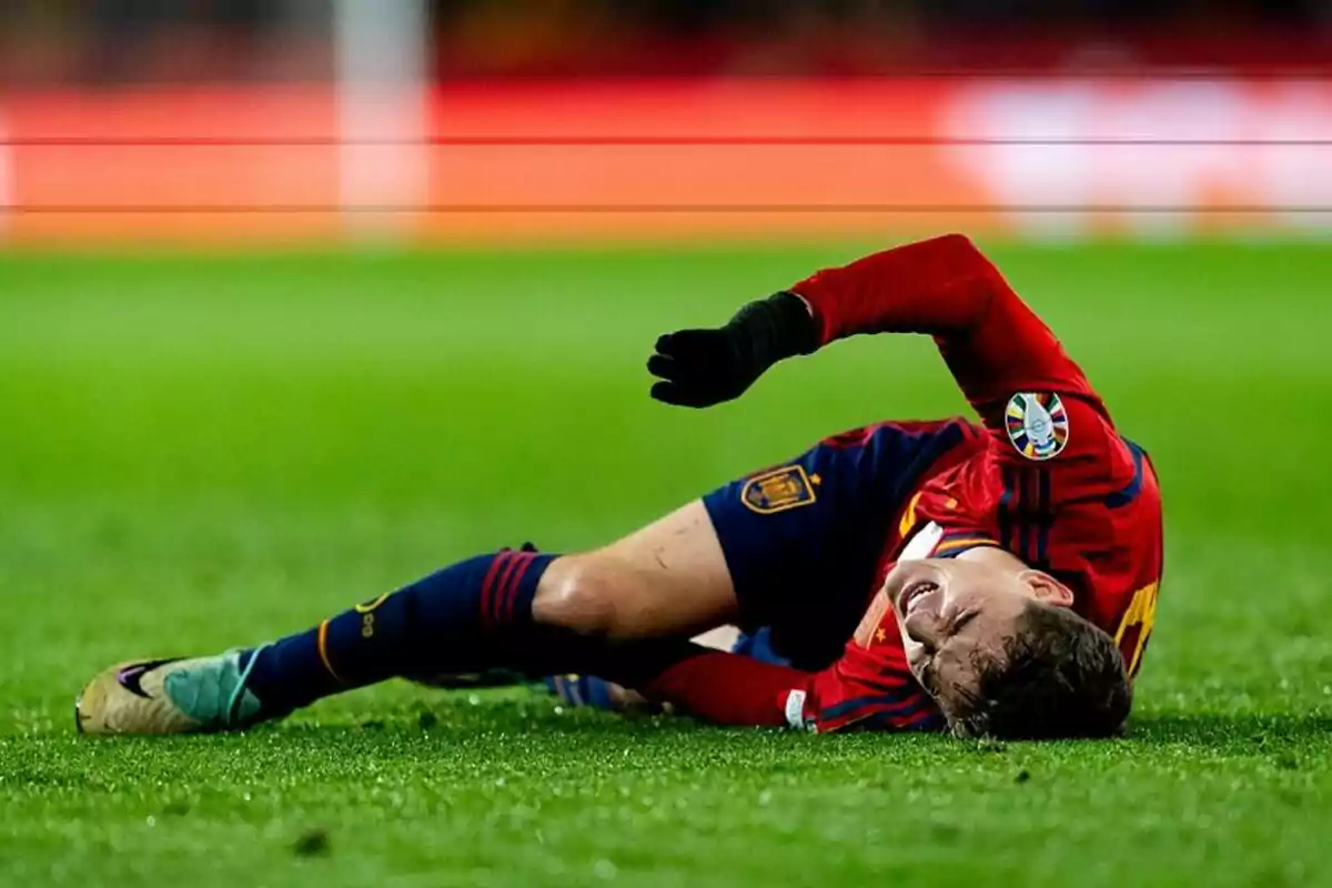 Jugador de fútbol con uniforme rojo y azul tendido en el césped, aparentemente lesionado.