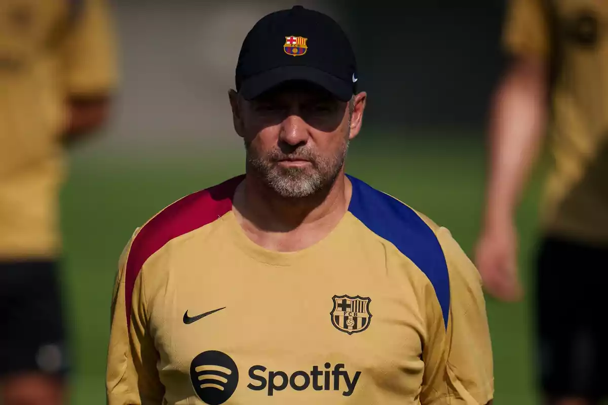 Hombre con gorra y camiseta del FC Barcelona en un campo de entrenamiento.