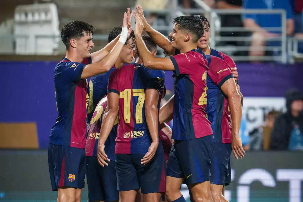 Jugadores de fútbol celebrando un gol con un choque de manos durante un partido bajo la lluvia.