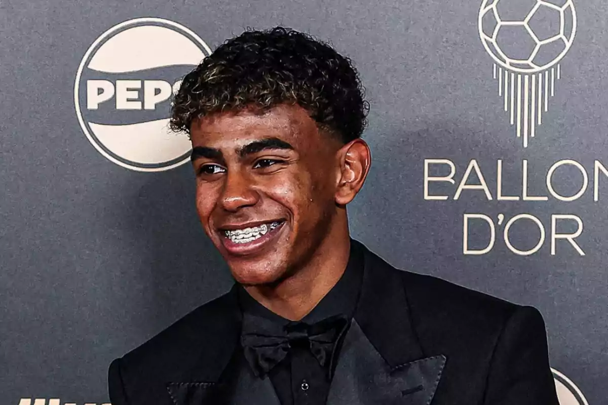 Un joven con traje negro y pajarita sonríe frente a un fondo con logotipos de Pepsi y Ballon d'Or.