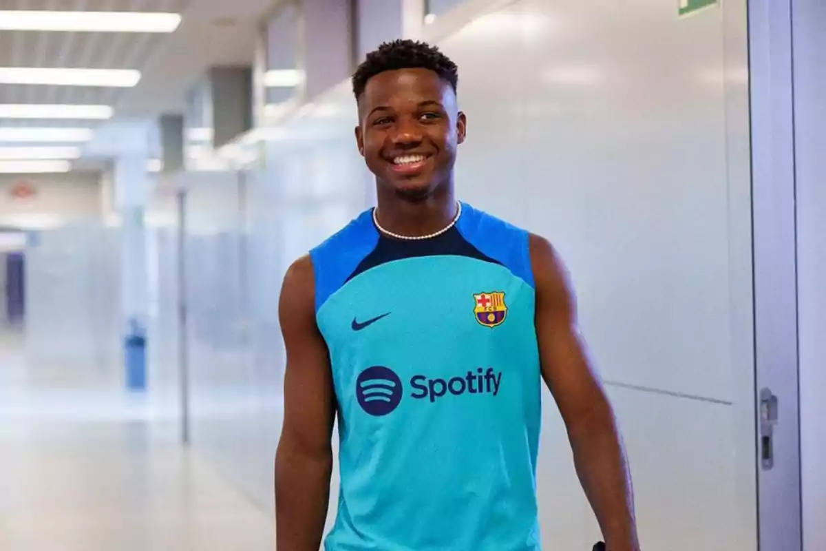 Un jugador de fútbol con una camiseta de entrenamiento del FC Barcelona sonríe mientras camina por un pasillo.