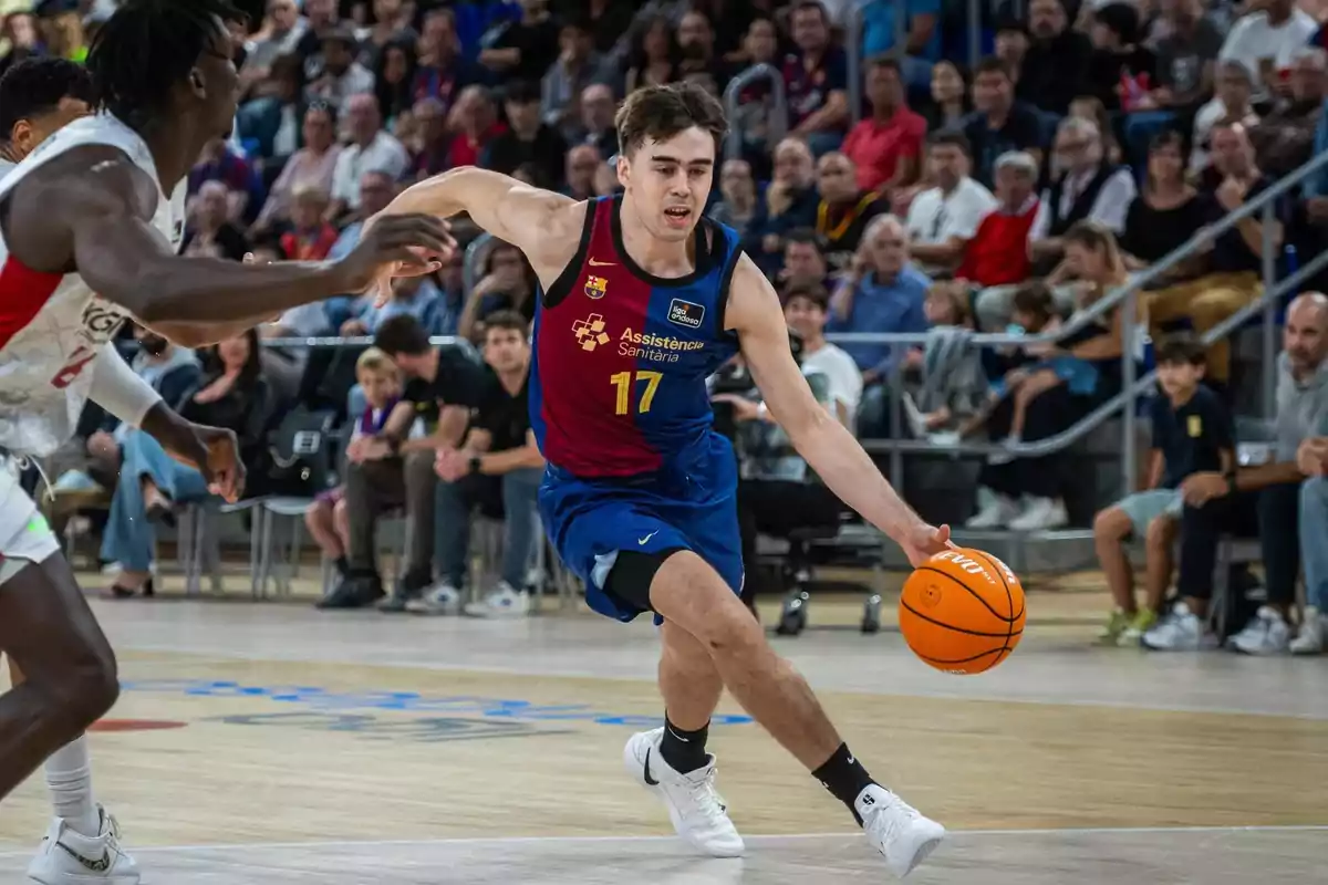 Jugador de baloncesto en acción durante un partido, driblando el balón mientras es perseguido por un oponente, con público en las gradas.