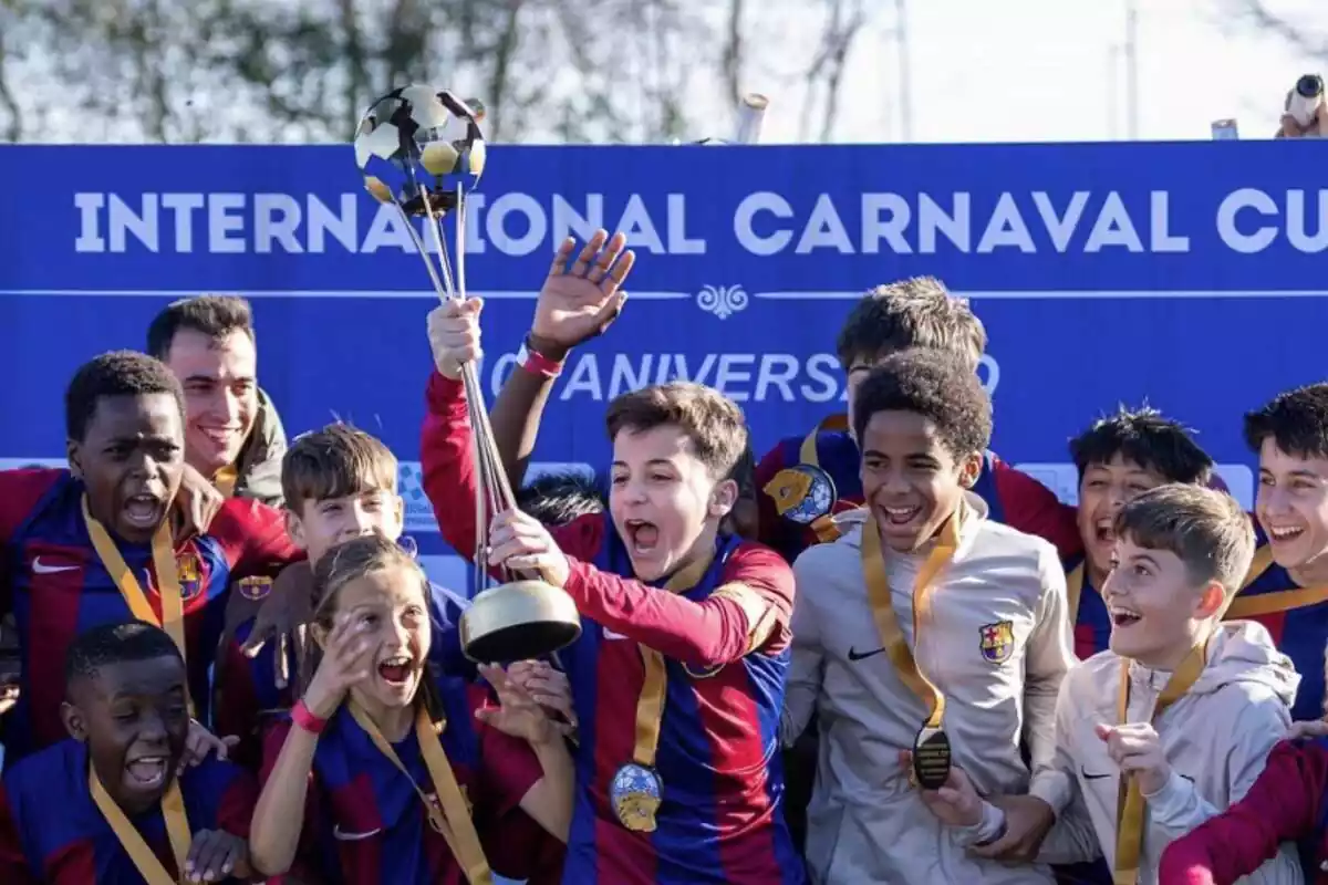 Jugadores del FC Barcelona en su categoría de menores levantan el trofeo de fútbol, con camisetas azulgranas y medallas amarillas.