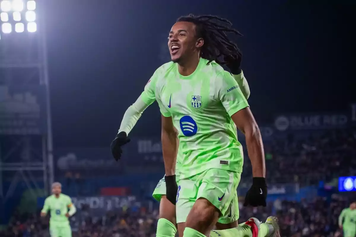 A soccer player in a green uniform celebrates on the field during a night game.