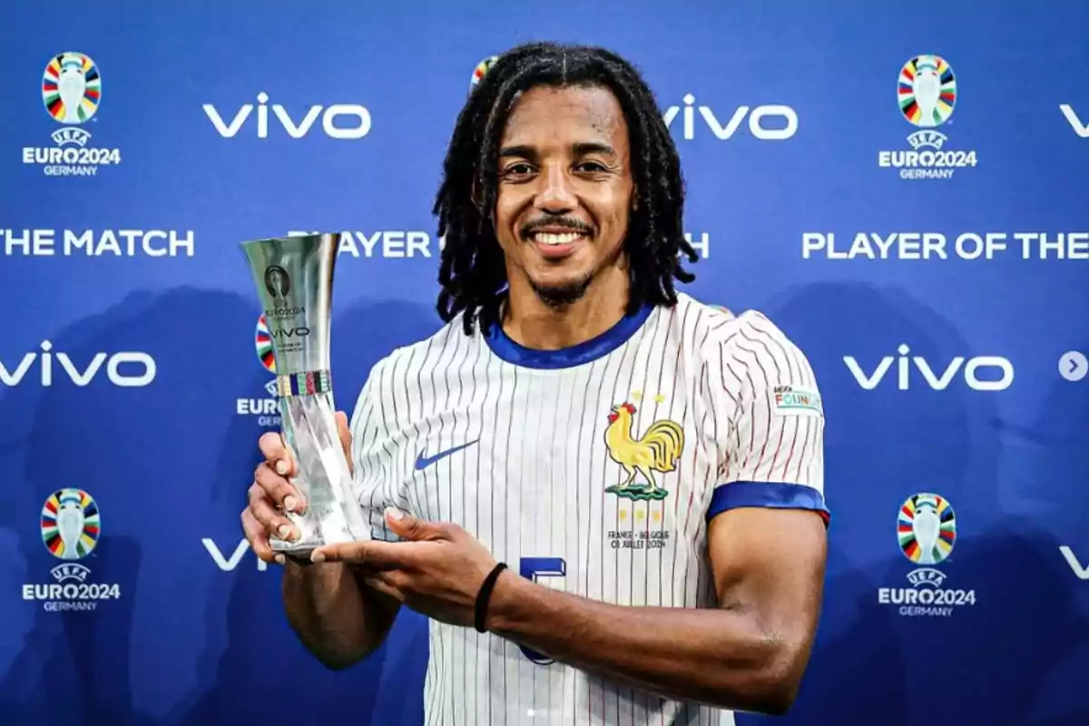 Un jugador de fútbol con una camiseta de la selección de Francia sostiene un trofeo frente a un fondo azul con logotipos de la UEFA Euro 2024 y Vivo.