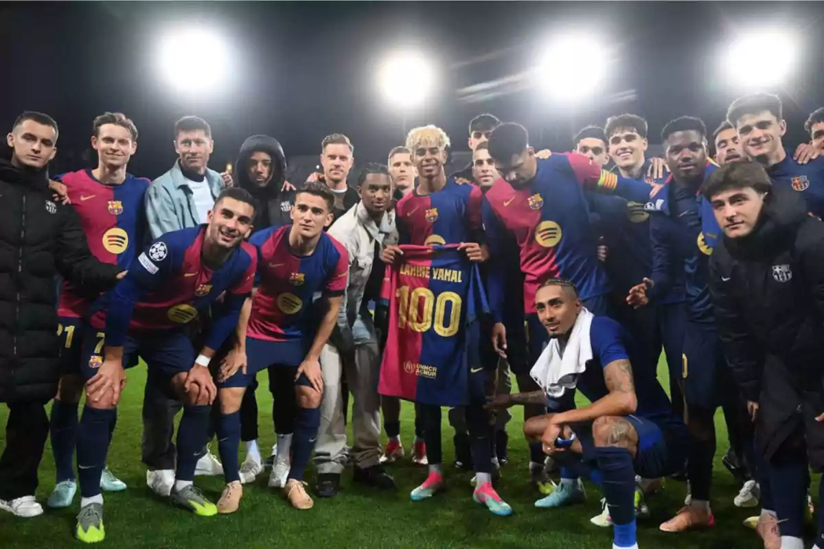 Un grupo de jugadores de fútbol del FC Barcelona posando juntos en el campo, uno de ellos sostiene una camiseta con el número 100. Un grupo de jugadores de fútbol del FC Barcelona posando juntos en el campo, uno de ellos sostiene una camiseta con el número 100.