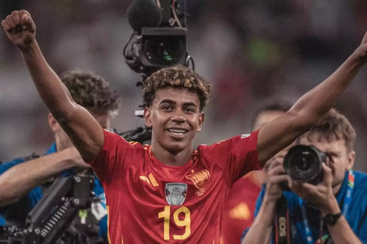 Jugador de fútbol celebrando con los brazos en alto mientras es fotografiado por la prensa.