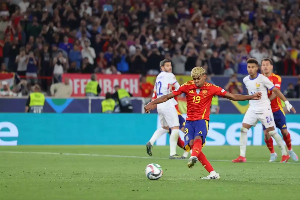 Jugador de la selección de España dispara el balón durante un partido de fútbol ante la selección de Francia con el público y fotógrafos al fondo Jugador de la selección de España dispara el balón durante un partido de fútbol ante la selección de Francia con el público y fotógrafos al fondo