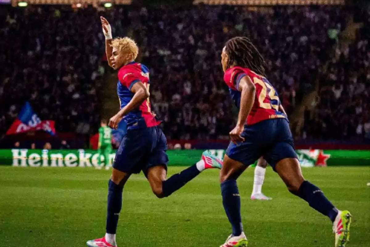 Dos jugadores de fútbol con uniforme azul y rojo celebran en el campo durante un partido. Dos jugadores de fútbol con uniforme azul y rojo celebran en el campo durante un partido.