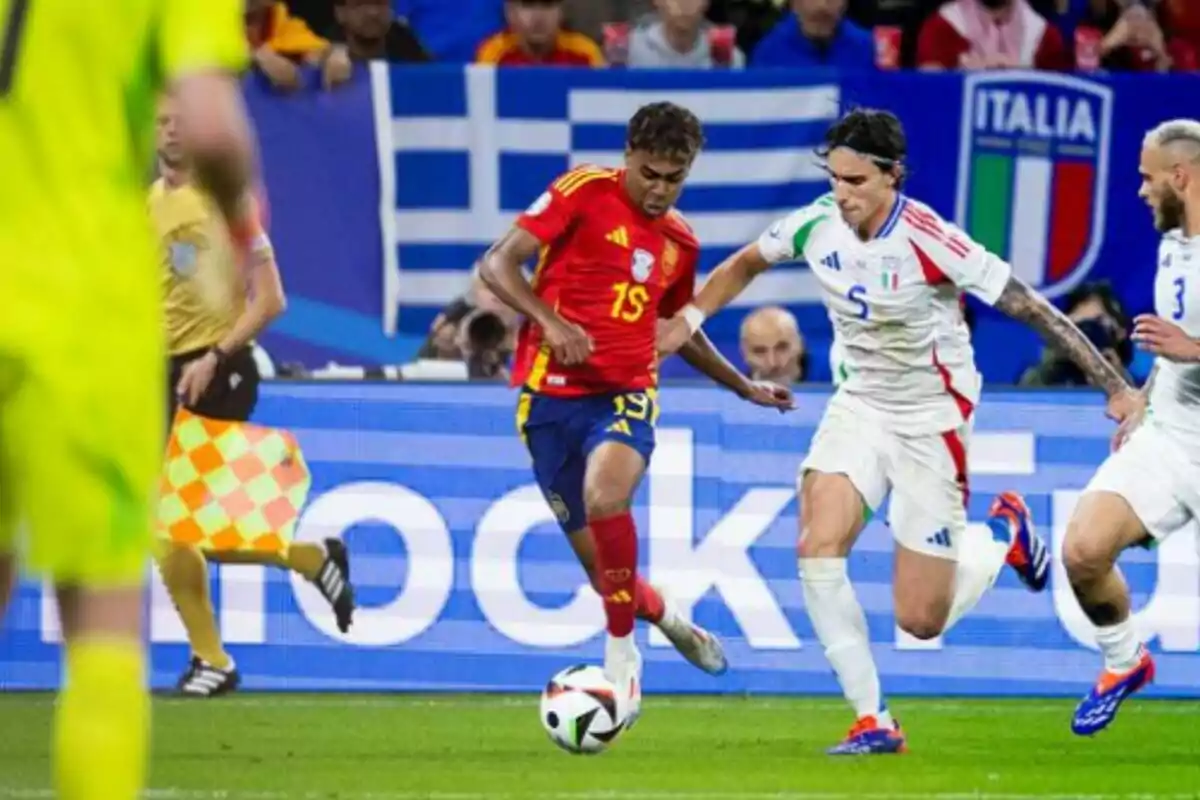 Jugadores de fútbol de los equipos de España e Italia compiten por el balón durante un partido, con un árbitro y un juez de línea observando.