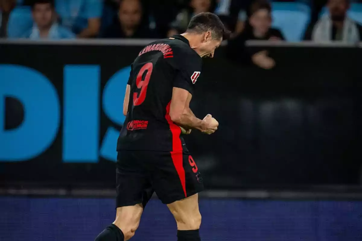 A soccer player celebrates with a clenched fist while wearing a black uniform with the number 9 on the back.