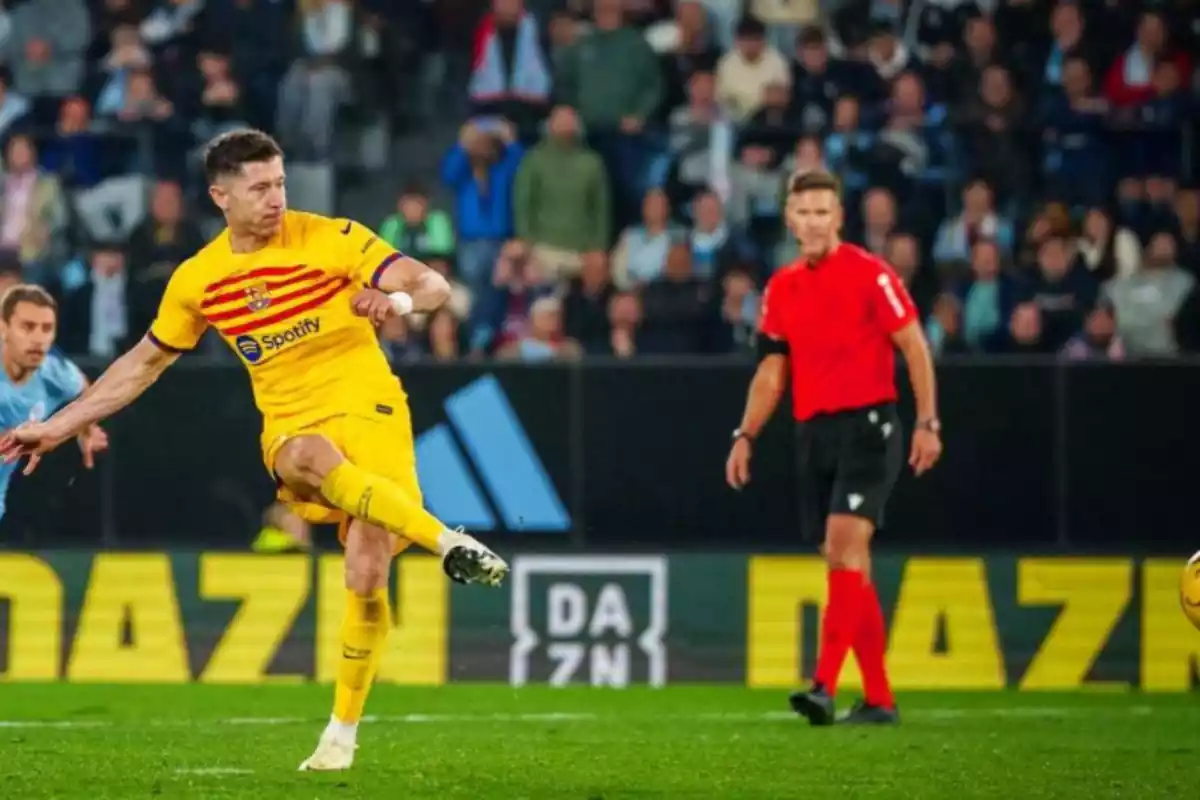 Se puede ver a un jugador vestido de amarillo, mientras golpea el balón. Está en una posición de disparo con la pierna arriba y el gesto serio.