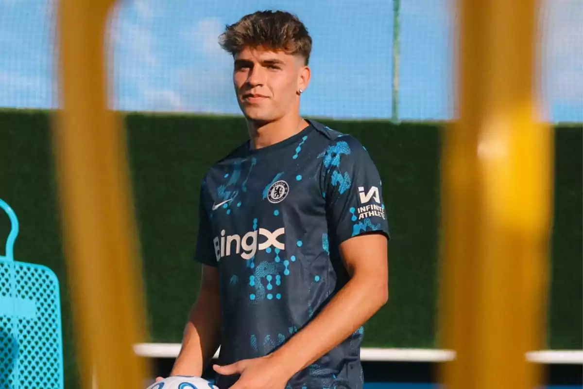 Soccer player in dark blue uniform holding a ball on a training field.