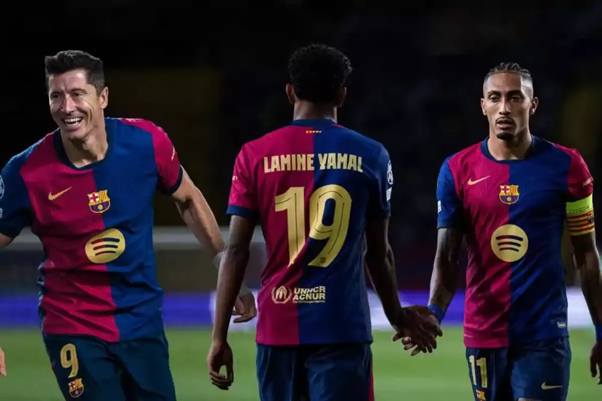 Tres jugadores de fútbol del FC Barcelona con uniformes azul y grana en el campo.