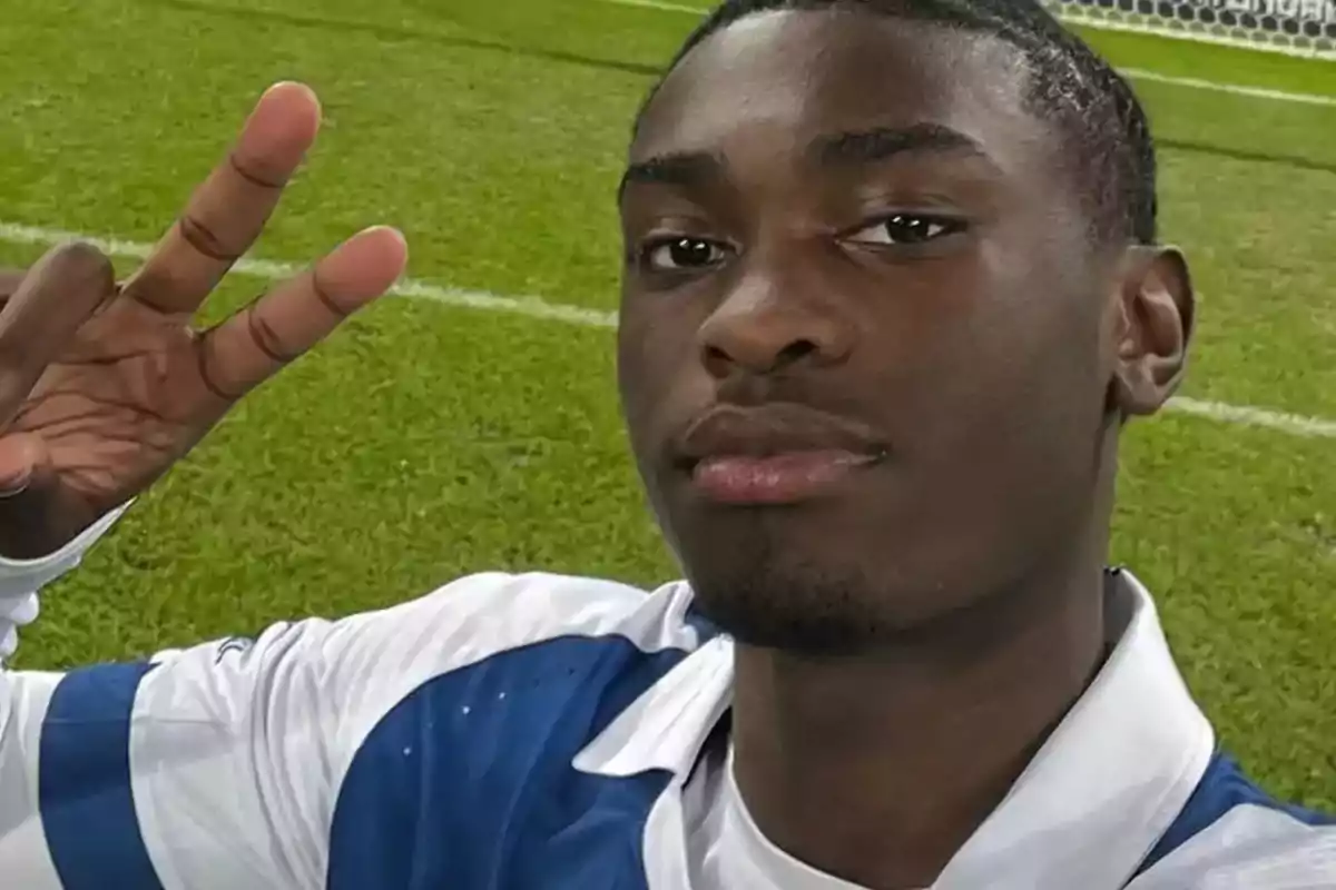 Una persona de color haciendose un selfie en un terreno de juego de futbol con los dedos en posición de v de victoria