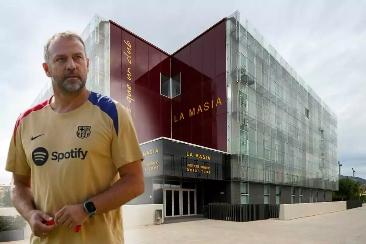 Un hombre con una camiseta del FC Barcelona está de pie frente a un edificio moderno con el letrero "La Masia".