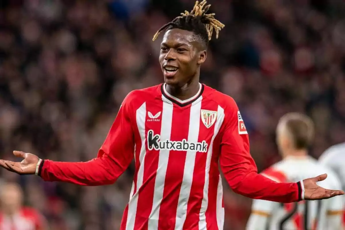 Un jugador de fútbol con el uniforme del Athletic Club de Bilbao gesticula con los brazos extendidos durante un partido.