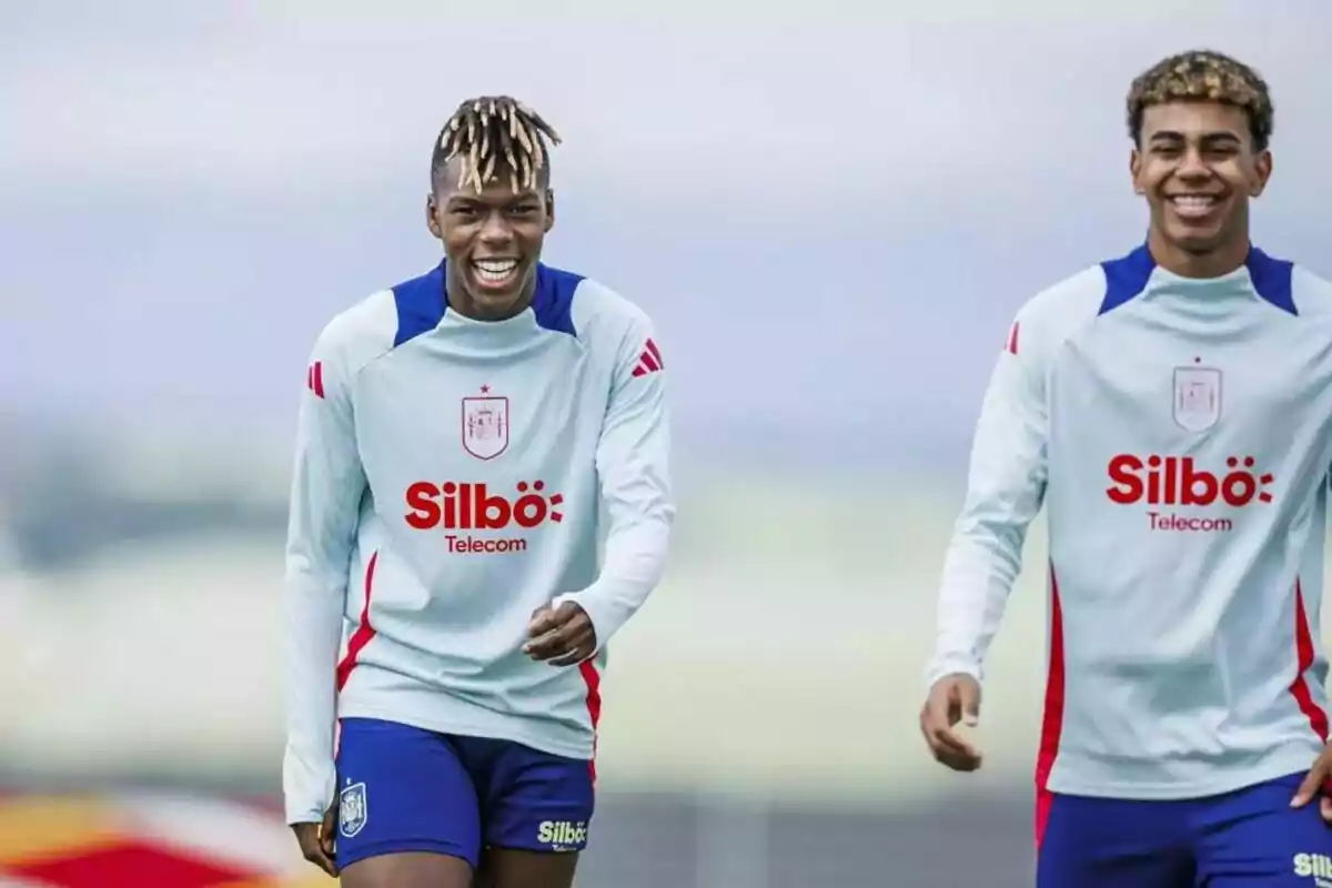 Dos futbolistas sonrientes con uniformes de entrenamiento blanco y azul de un equipo patrocinado por Silbö Telecom.