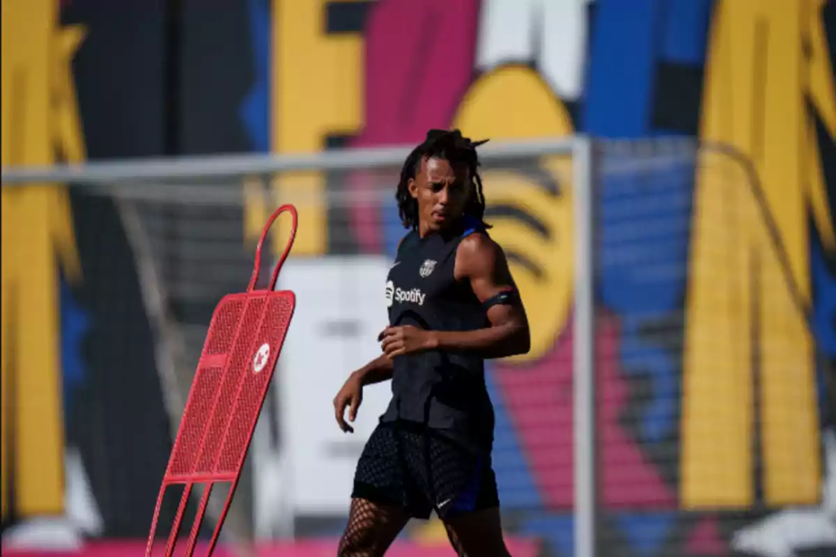 Jugador de fútbol entrenando en un campo con un maniquí de entrenamiento rojo y un mural colorido de fondo.