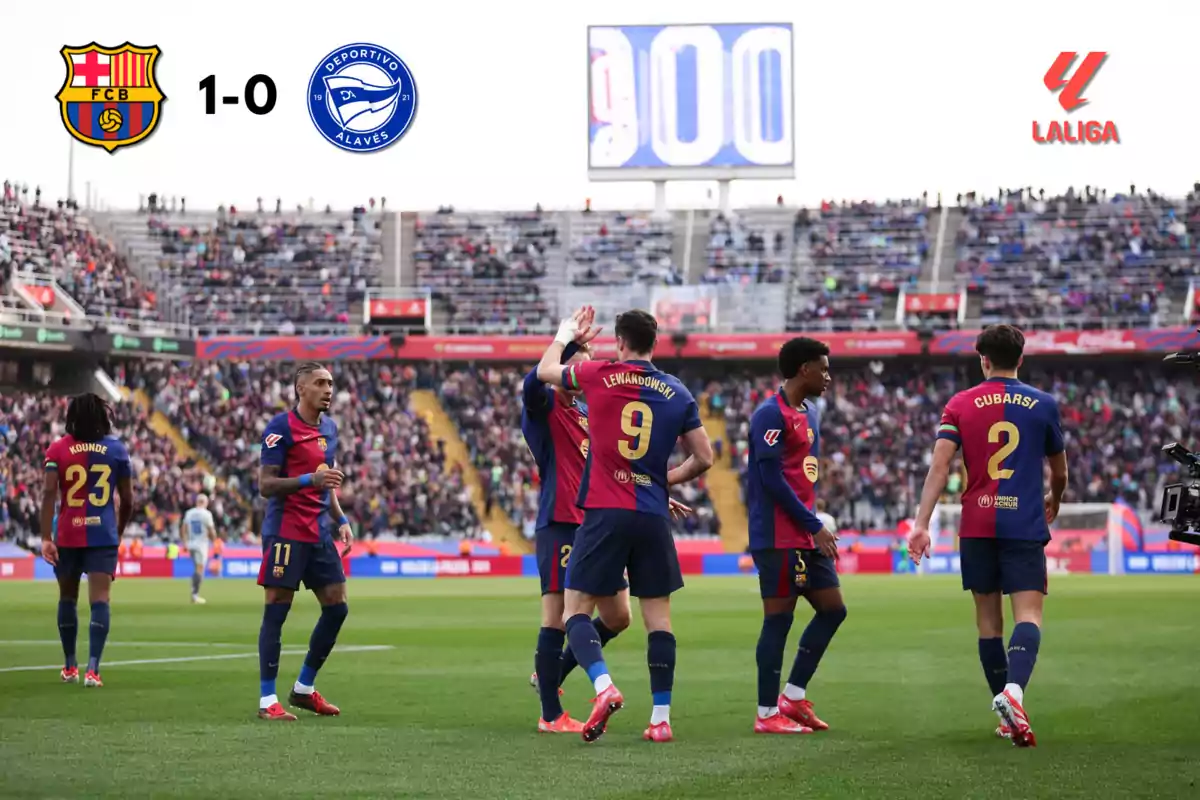 Jugadores de un equipo de fútbol celebran un gol en un estadio lleno de espectadores, con el marcador mostrando 1-0 a favor del equipo local.