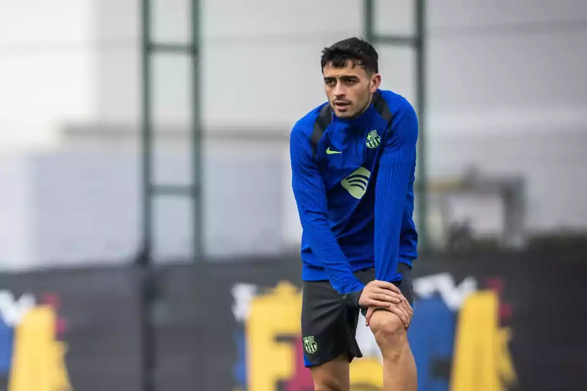 A soccer player in a blue and black training uniform leans forward on a sports field.