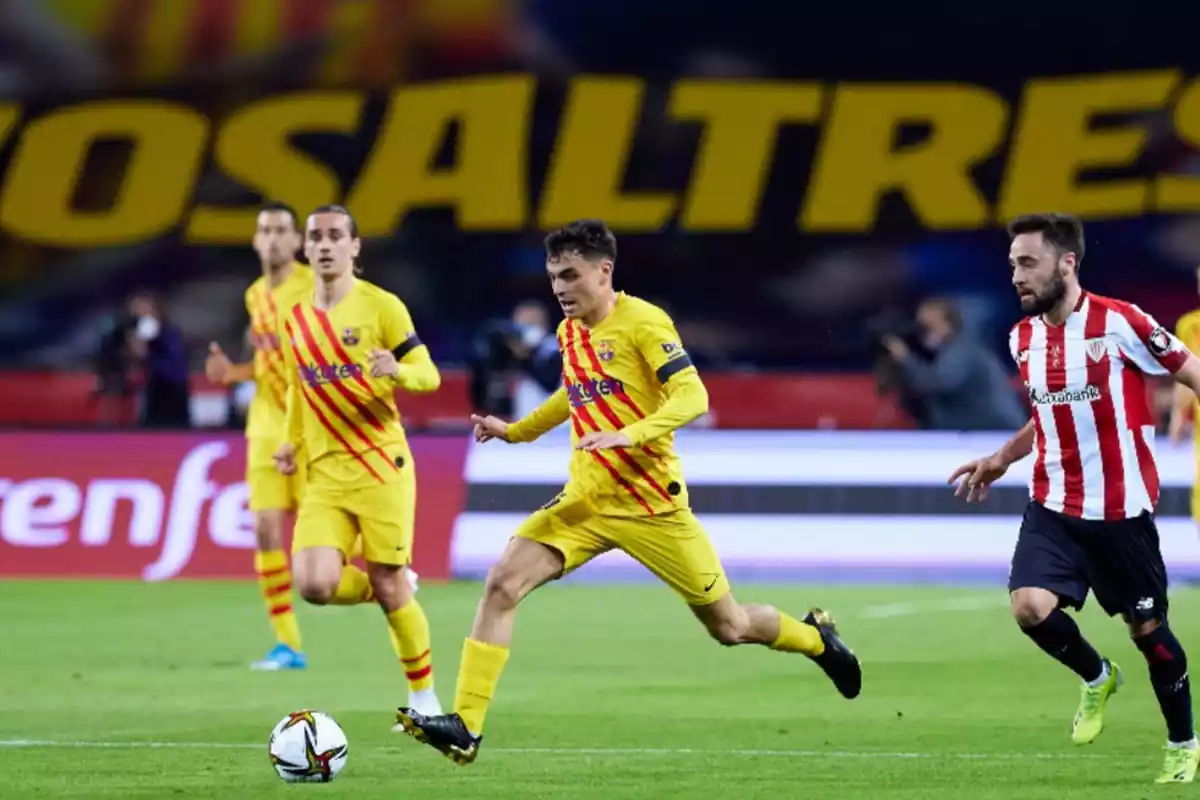 El jugador del Barça Pedri en el campo conduciendo una pelota, con un jugador del Athletic detrás de él