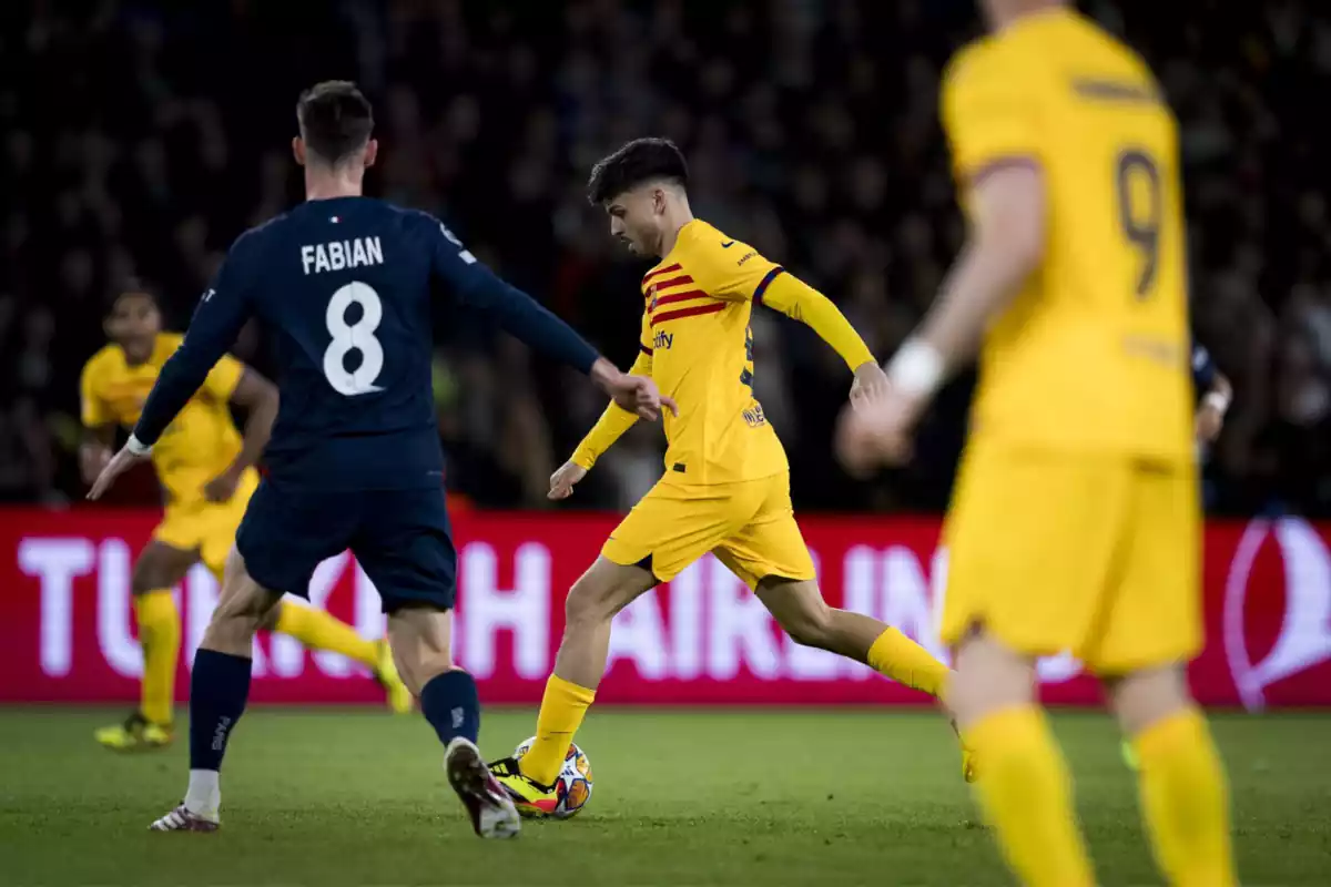 Pedri con la equipación amarilla del Barça controlando el balón con la pierna izquierda junto a Fabián Ruiz con el dorsal 8 a la espalda de la camiseta azul del PSG