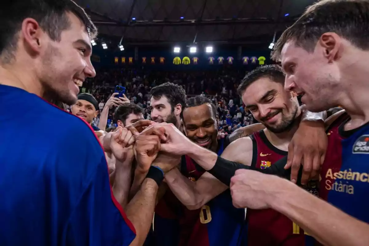 Jugadores de baloncesto celebrando en equipo con sonrisas y gestos de camaradería en una cancha llena de espectadores.