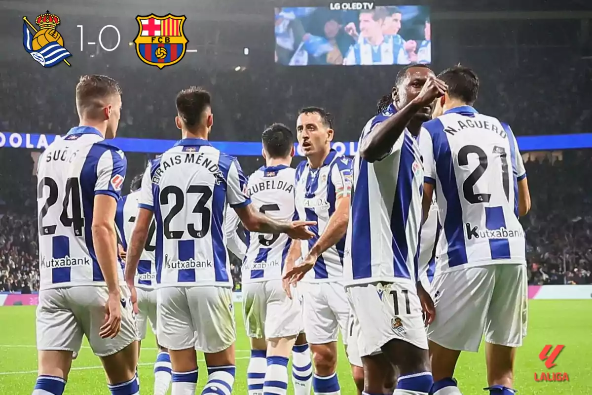 Jugadores de la Real Sociedad celebran un gol en un partido contra el FC Barcelona, con el marcador mostrando 1-0 a favor de la Real Sociedad en un estadio iluminado.