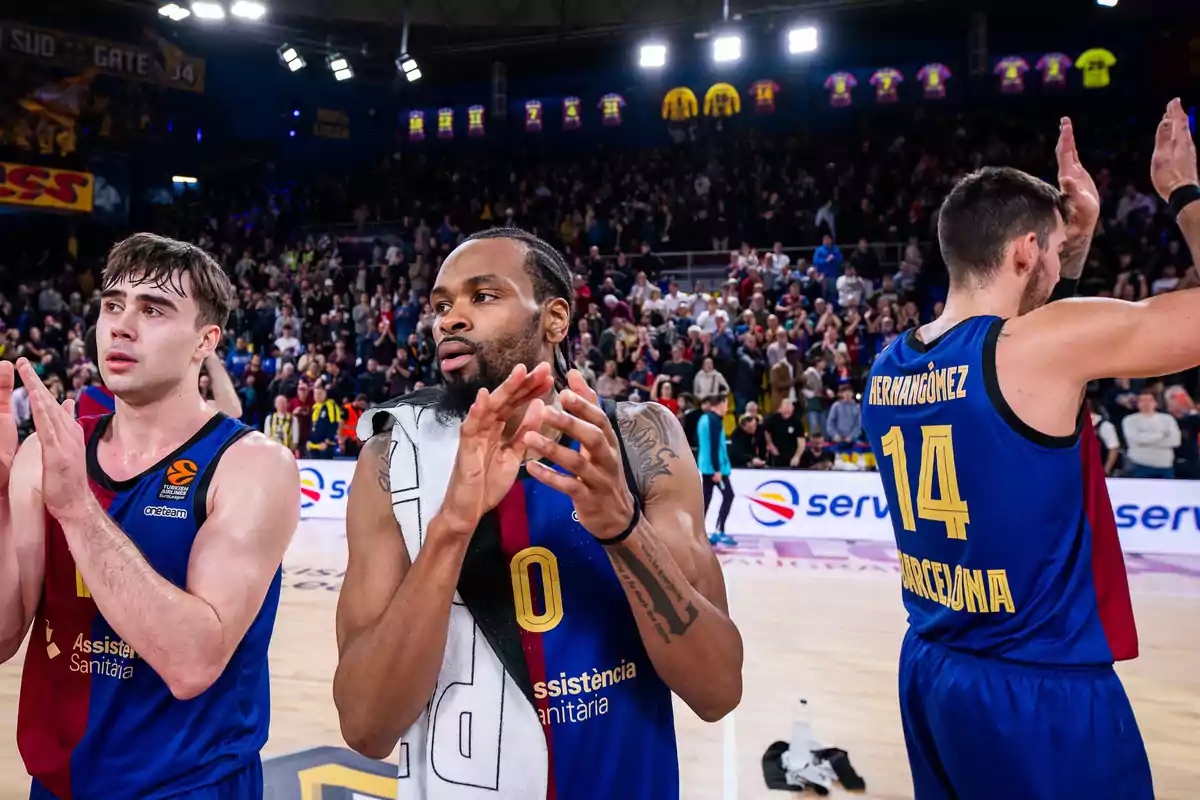 Jugadores de baloncesto aplaudiendo en la cancha después de un partido, con el público de fondo.