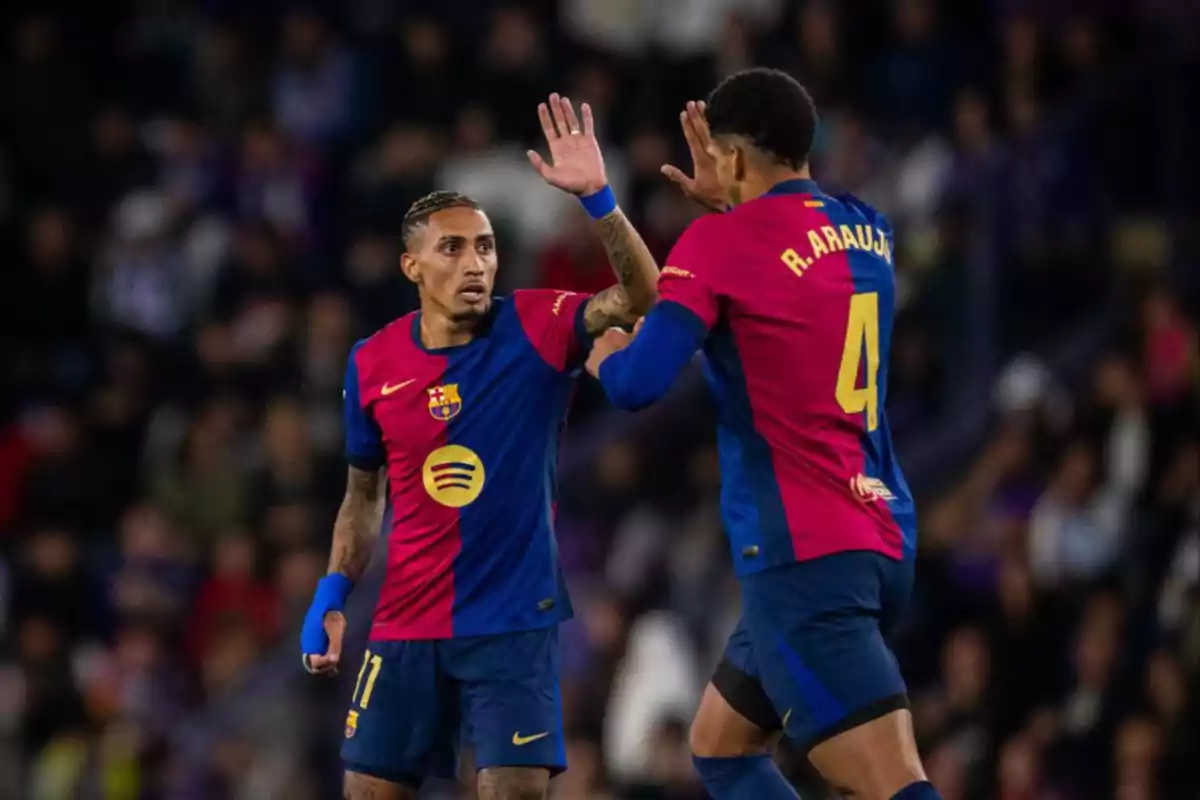 Two players from FC Barcelona celebrate on the field with a handshake, wearing the team's uniform. Two players from FC Barcelona celebrate on the field with a handshake, wearing the team's uniform.