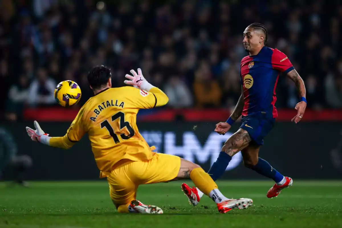 A player in a blue and red uniform tries to score while the goalkeeper in a yellow uniform dives to stop the ball.