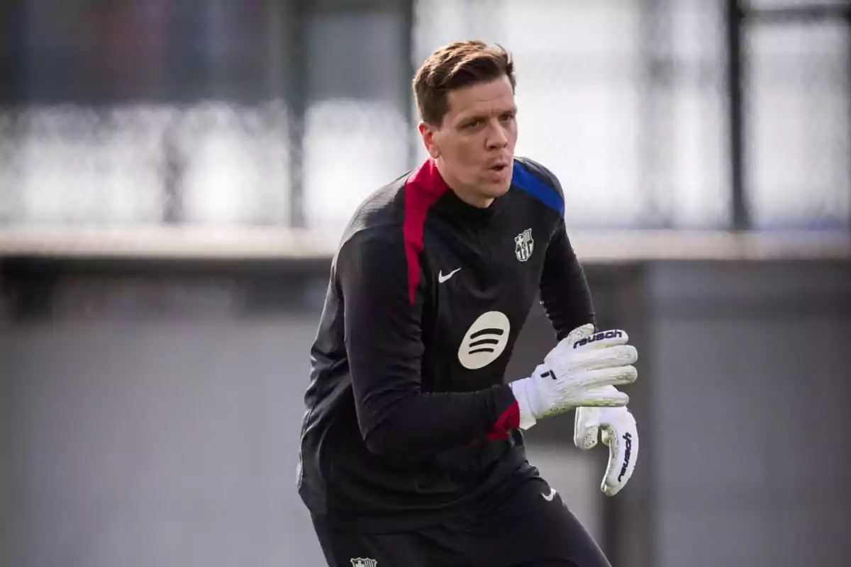 A soccer goalkeeper wearing white gloves and a black training uniform prepares to catch the ball on an outdoor field. A soccer goalkeeper wearing white gloves and a black training uniform prepares to catch the ball on an outdoor field.