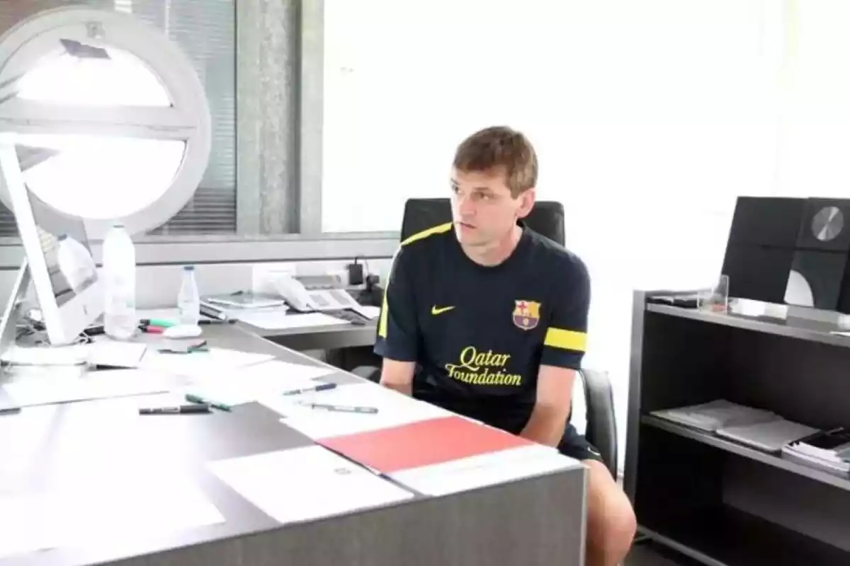 Tito Vilanova sentado en una mesa con muchos documentos en la mesa y evestido con una camiseta negra del Barça