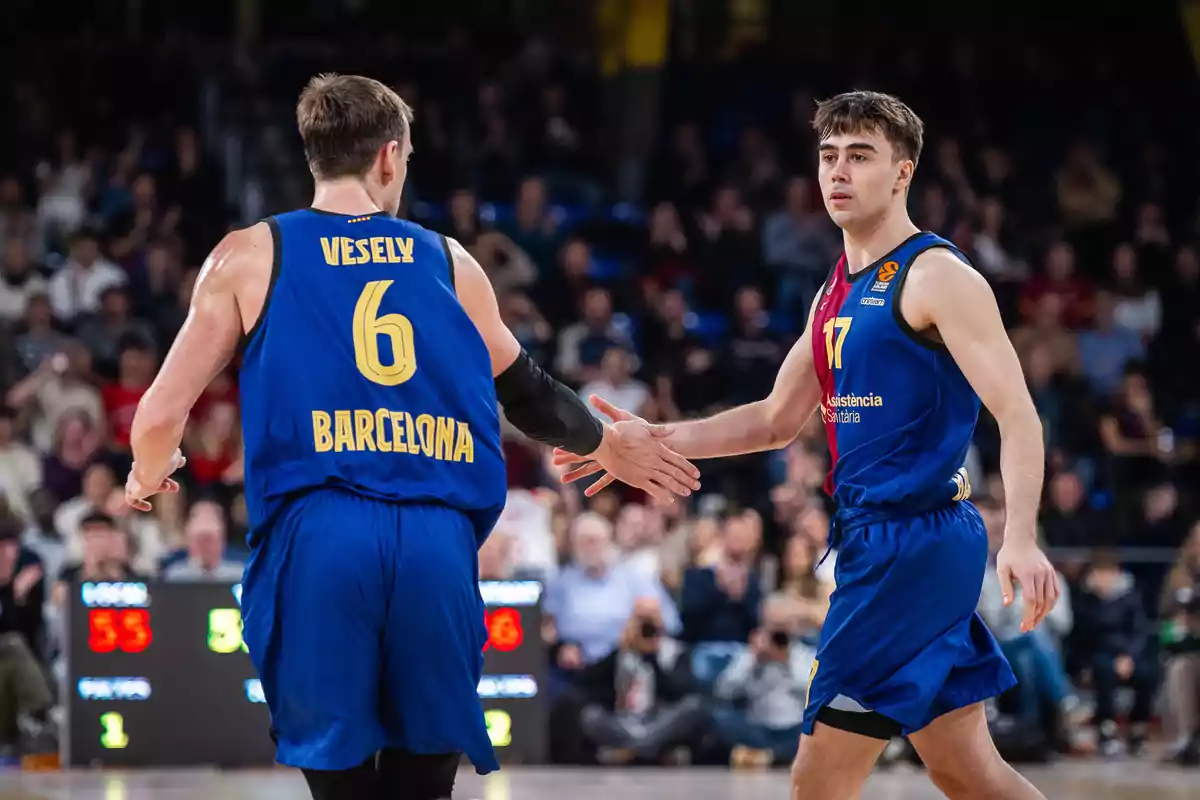 Dos jugadores de baloncesto del equipo Barcelona se dan la mano en la cancha durante un partido.