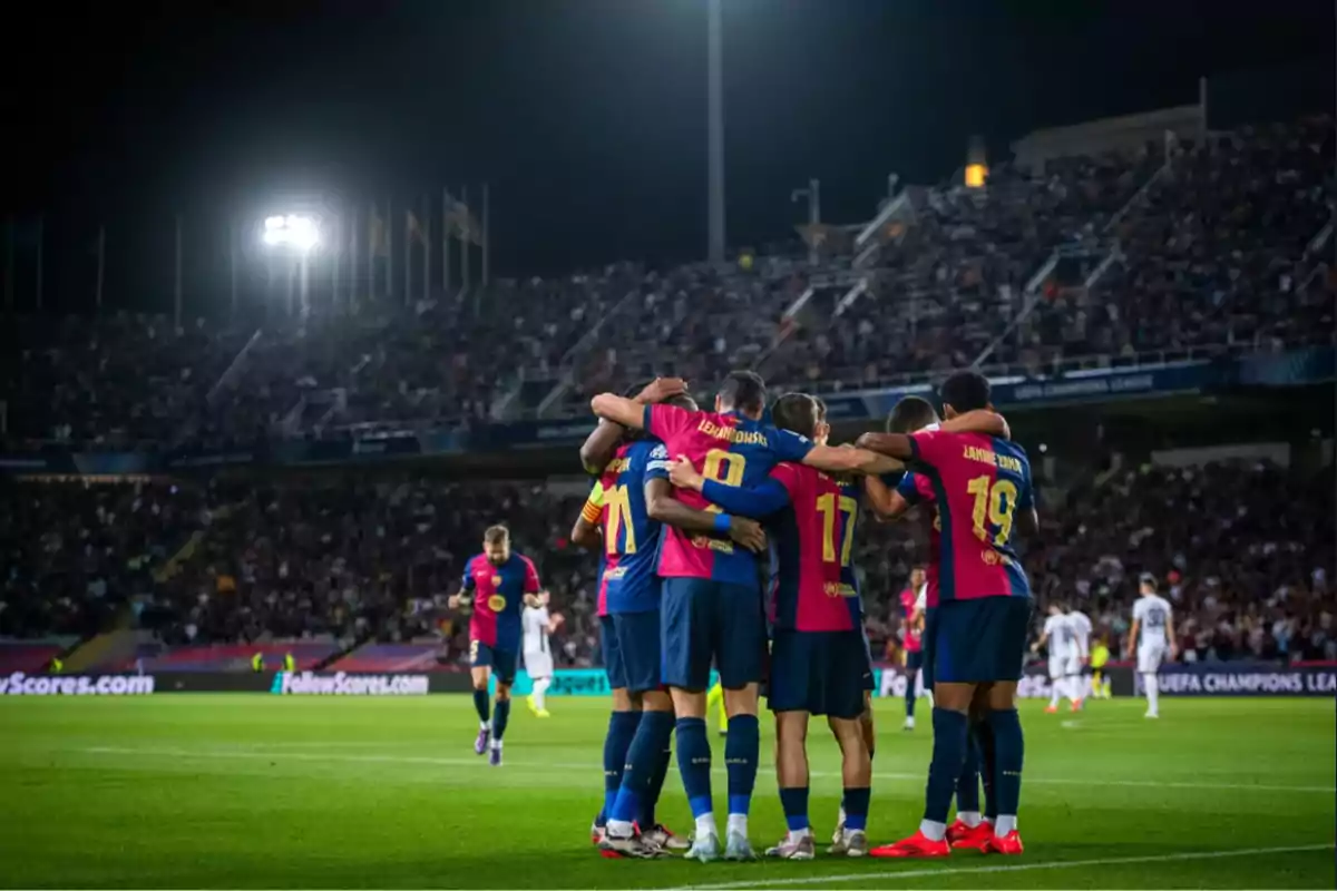 Jugadores de fútbol celebrando en grupo en un estadio iluminado durante un partido nocturno.