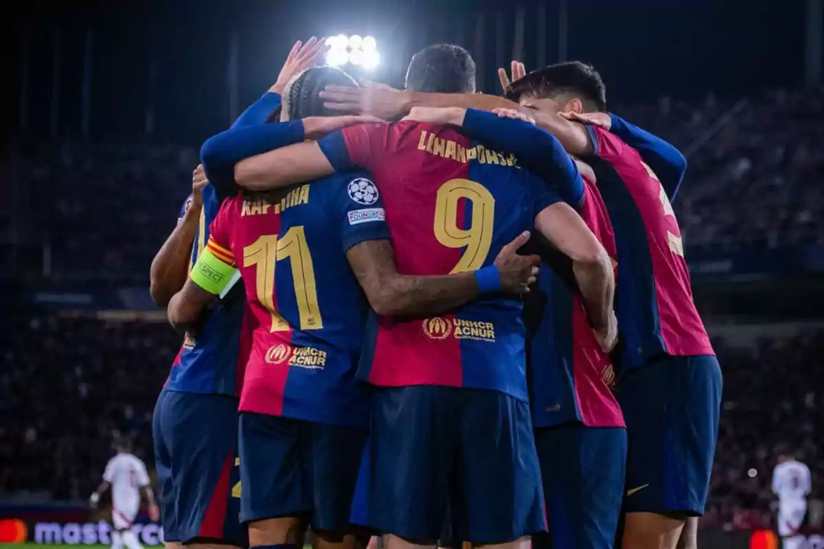 Jugadores de fútbol celebrando un gol en equipo durante un partido nocturno.