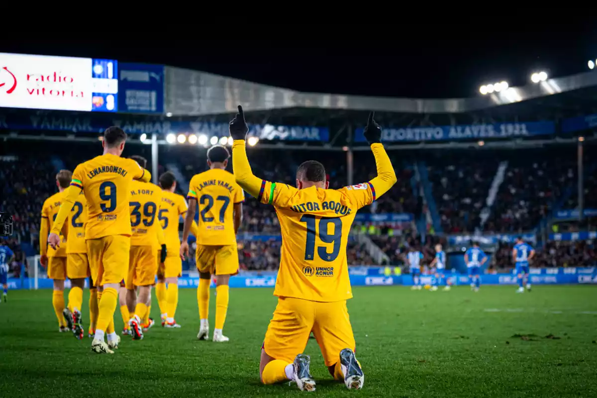 El jugador del Barça Vitor Roque celebrando un gol de rodillas en el campo con los dedos apuntando al cielo