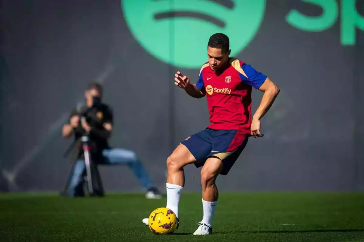 Vitor roque entrenando con la indumentaria roja, azul y dorada del FC Barcelona y un balón amarillo en sus pies