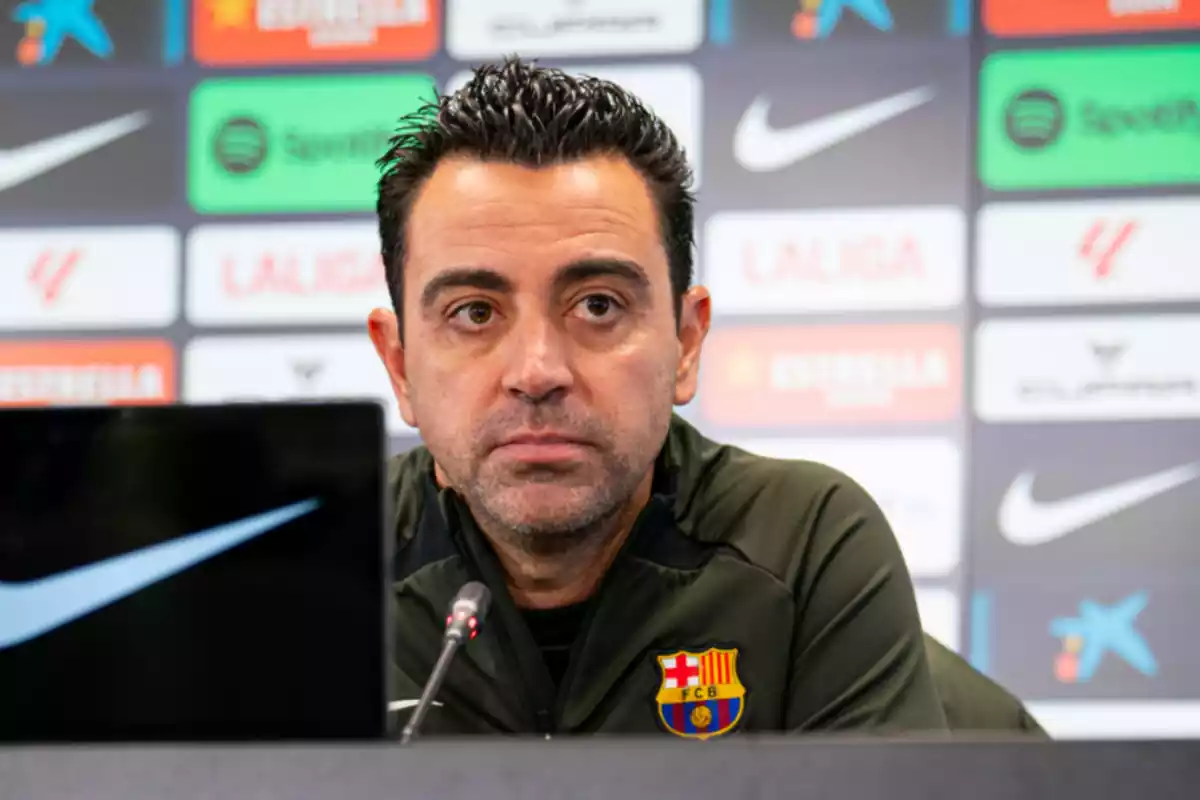 xavi en rueda de prensa se muestra con un rostro serio, una camiseta verde oscuro con el escudo del barcelona en el pecho