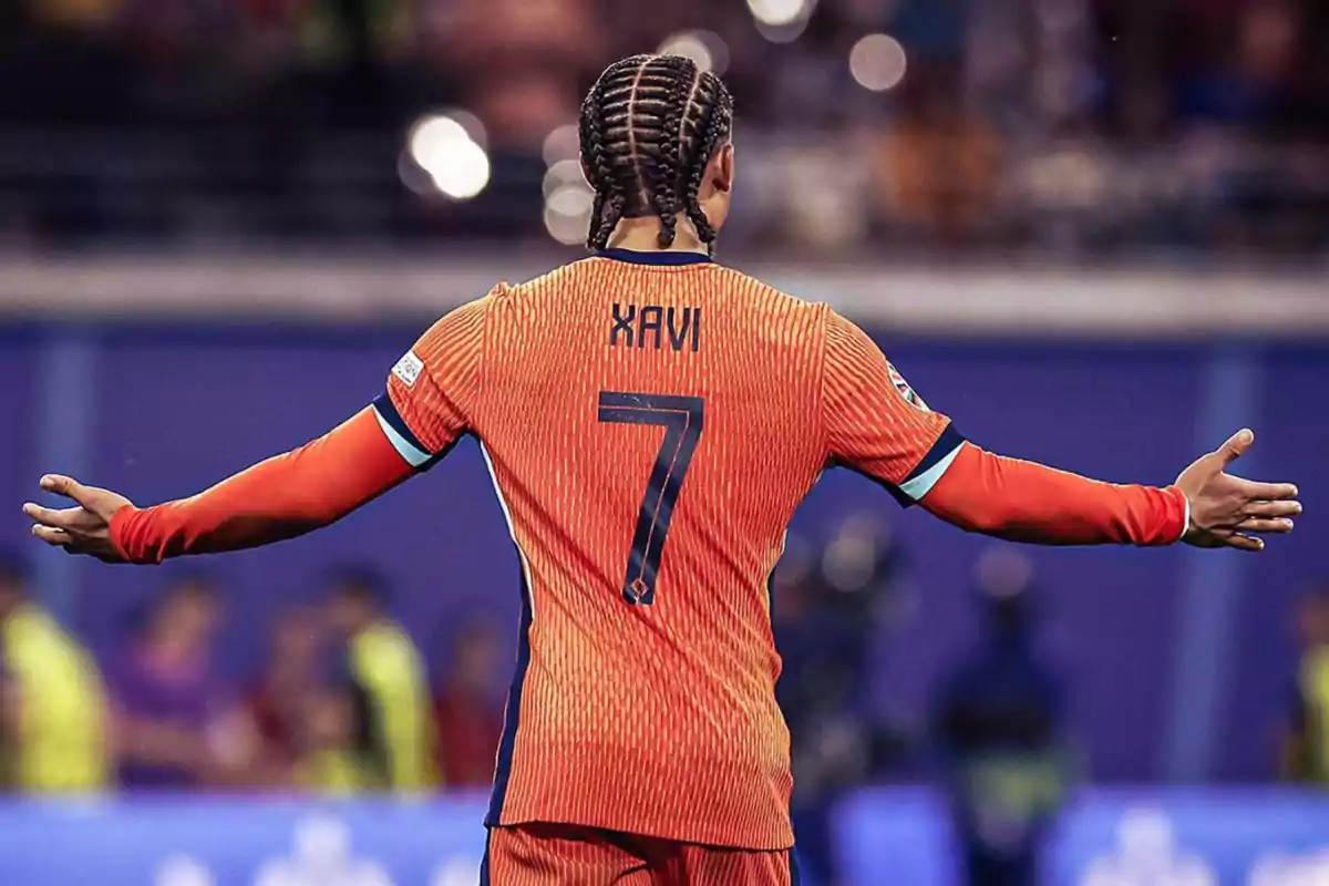 Jugador de fútbol con trenzas y camiseta naranja con el nombre "Xavi" y el número 7 en la espalda, con los brazos extendidos en un estadio.